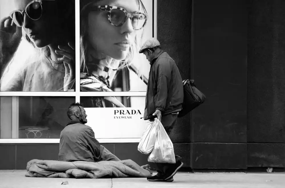 Un homeless davanti la vetrina di Prada, simbolo crisi di valori sociali